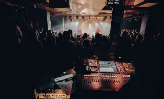 Photo de concert avec la scene dans le fond, et en premier plan la console de la régie