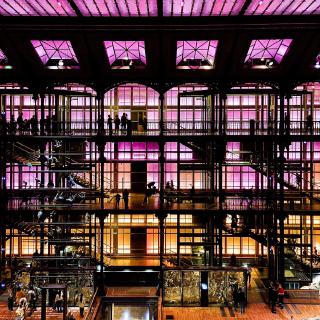 La vue interne d'un bâtiment avec 4 étages qui vont de l'orange au magenta. Le style est proche de l’époque victorienne