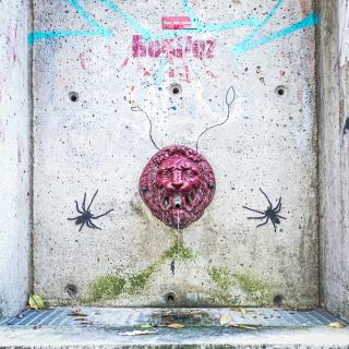 Fontaine à eau en forme d'une tete de lyon cerné par deux araignées peinte sur le mur