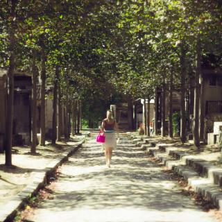Une femme avec un sac rose marche au loin dans le [Cimetière du Père-Lachaise](https://fr.wikipedia.org/wiki/Cimeti%C3%A8re_du_P%C3%A8re-Lachaise)