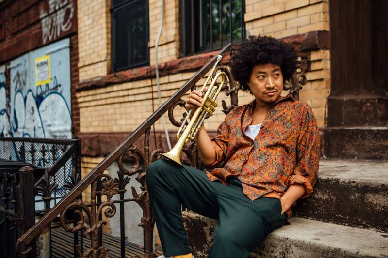Takuya Kuroda assis sur le perron d'un immeuble, possiblement à New York, tenant sa trompette
